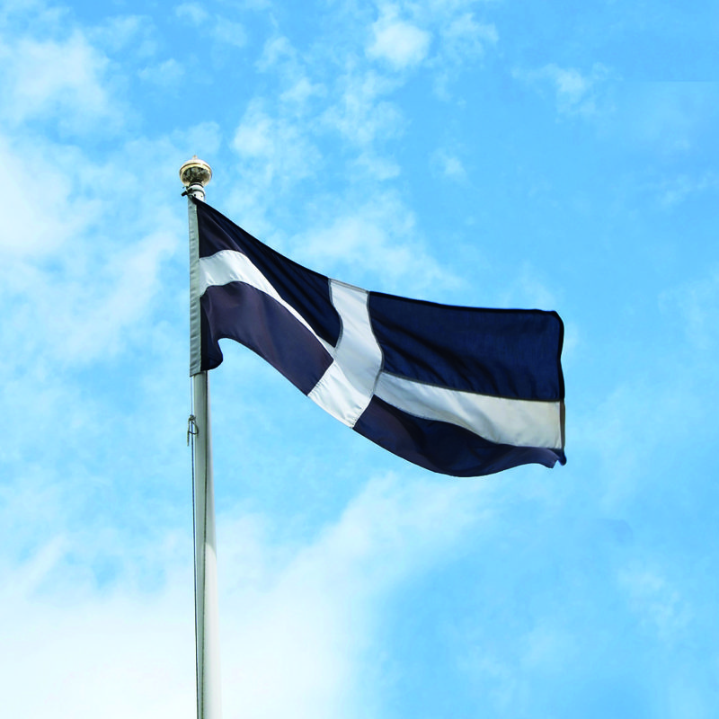 Cornish flag flying on a flagpole with a blue sky in the background